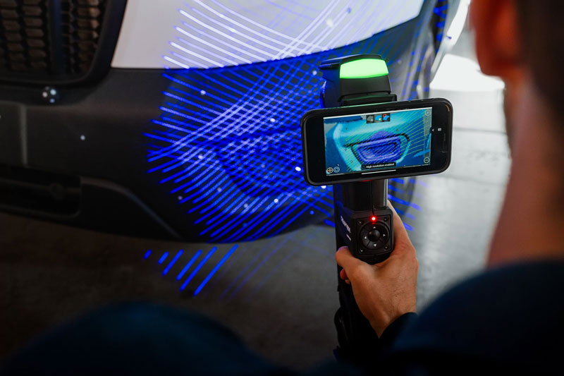 Close-up of a HandySCAN MAX 3D scanner used to measure the front of a white van while the scan is displayed on an attached cellphone with remote desktop VXmodel