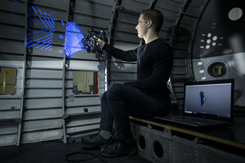 Engineer scanning the interior of an aircraft fuselage with a MetraSCAN 3D scanner with a laptop on his side displaying the 3D scan data.