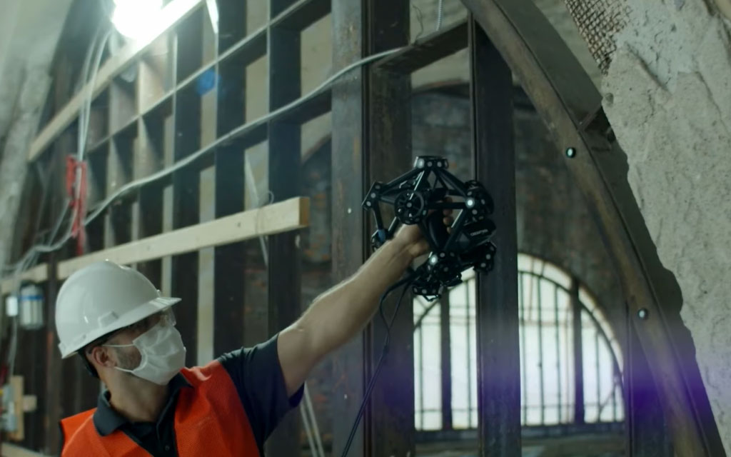Worker wearing a white hard hat and orange safety vest scanning a damaged stone arc with the MetraSCAN 3D scanner