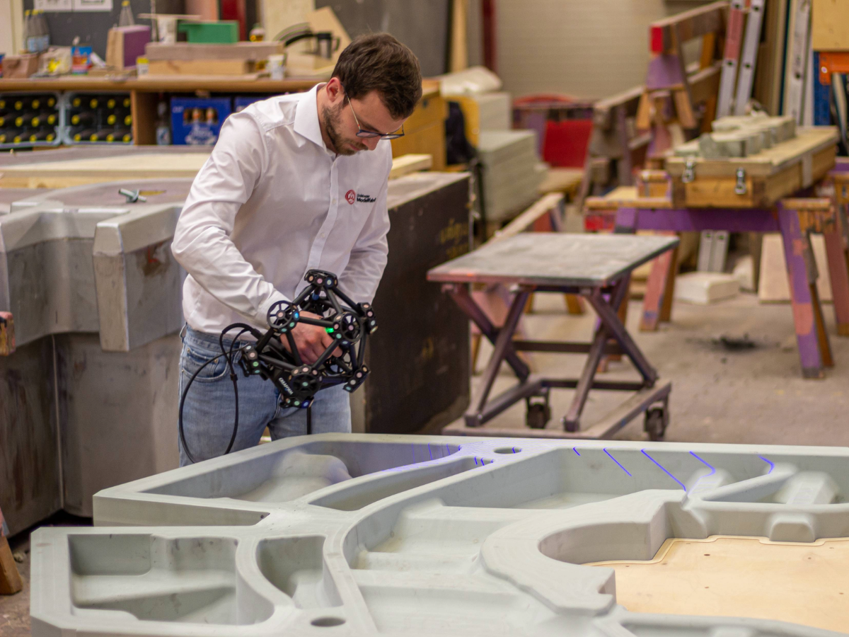 Man in a white shirt using a MetraSCAN 3D to measure a large mold in a workshop.