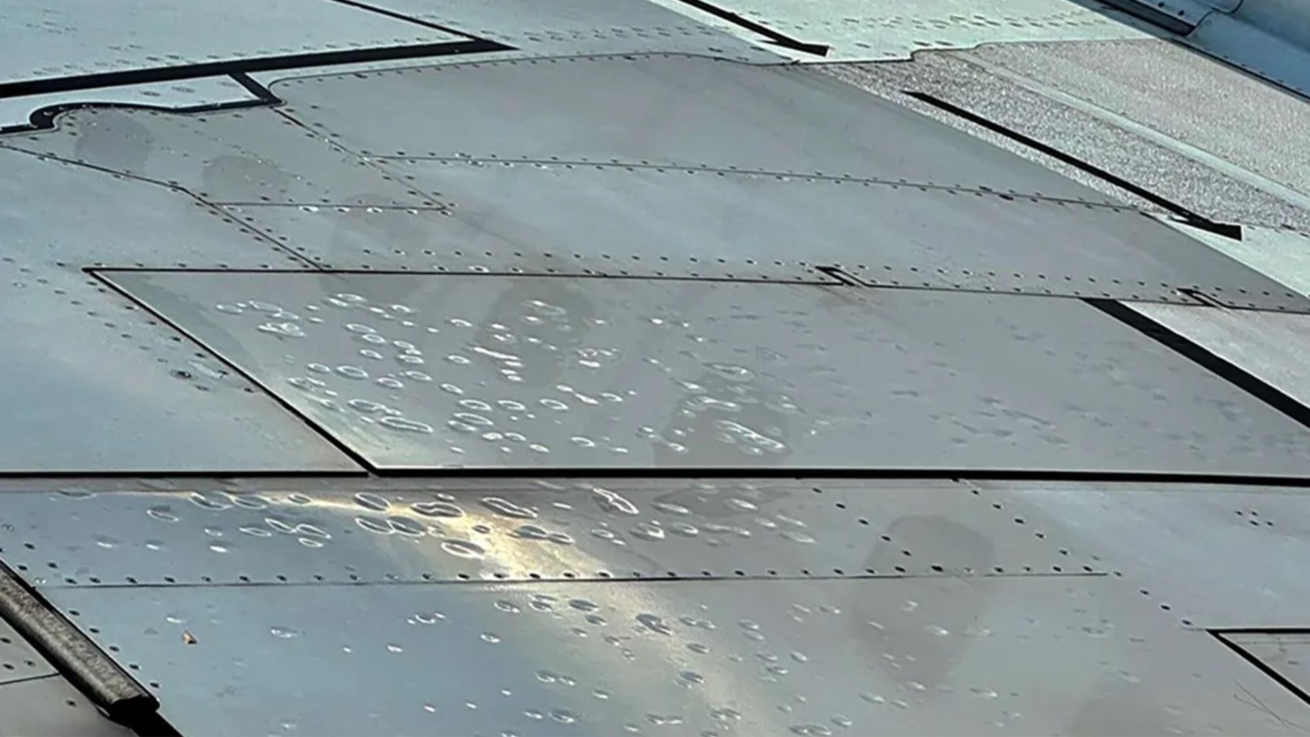 Close-up of a plane whing with several dents caused by a hailstorm.