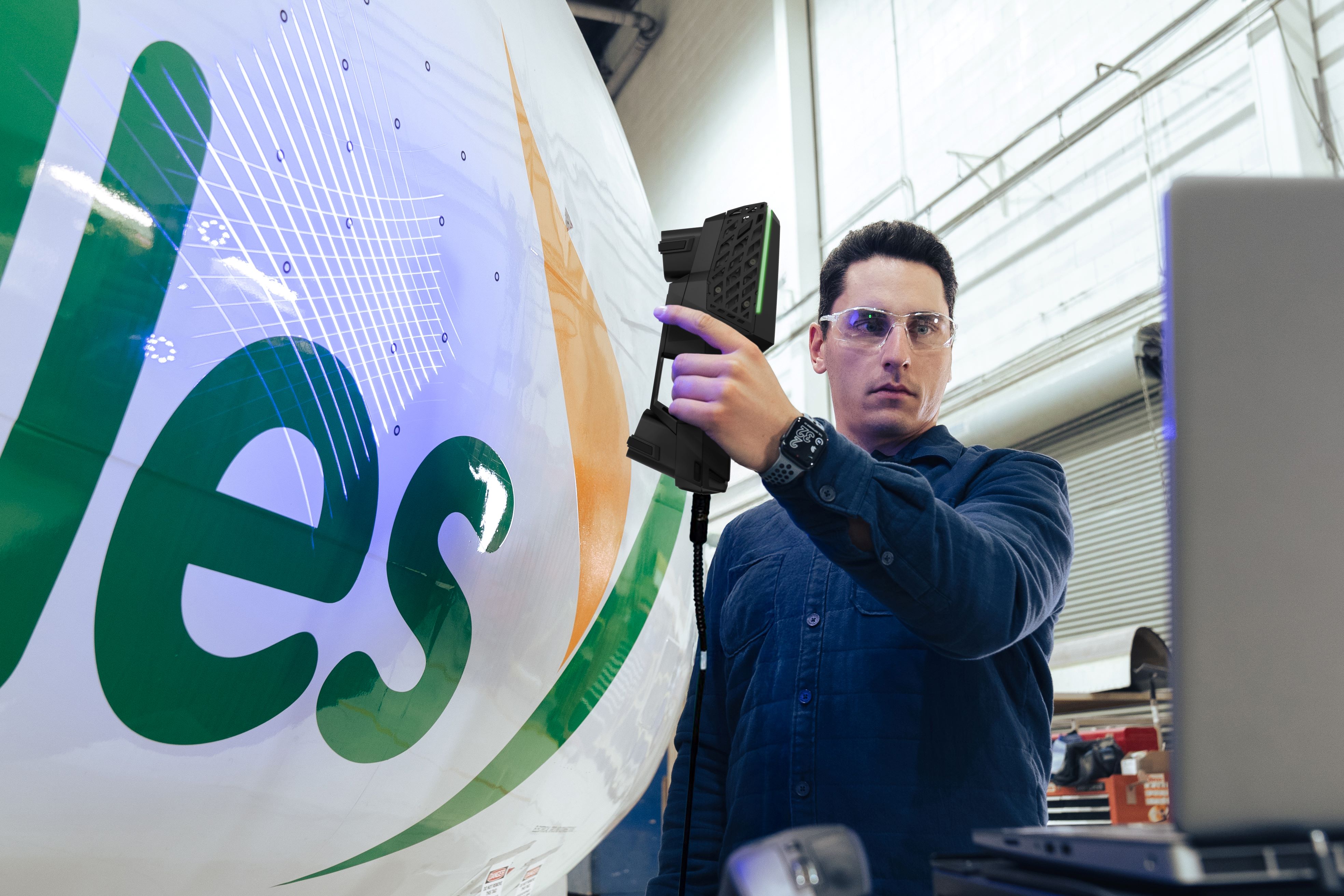Technician using the HandySCAN EVO Elite scanner to scan the side of a white plane while looking at the results on a laptop screen.
