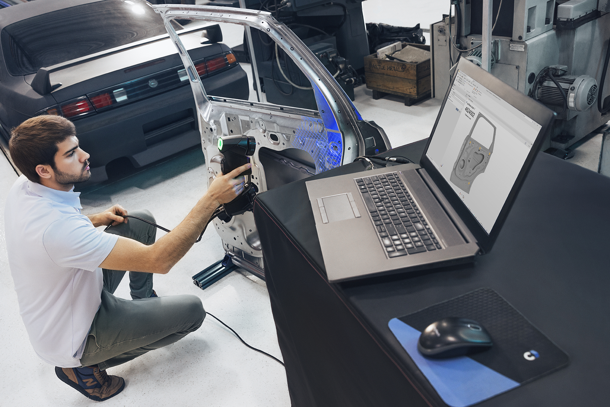 Man using the HandySCAN BLACK Elite to scan the interior of a detached car door next to a desk with a laptop displaying the scan in PolyWorks.