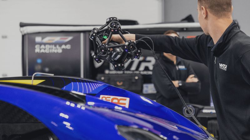 Engineer from WTR team scanning the surface of a blue Cadillac GTP race car with a Creaform MetraSCAN 3D scanner in preparation for scrutineering.