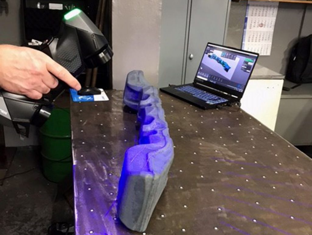 HandySCAN 3D BLACK used to scan forged component on a table with laptop in the background displaying VXelements