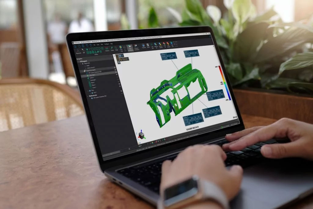 Close-up of a laptop on a desk displaying the 3D model of a stamped part in the VXinspect module with GD&T symbols around the part