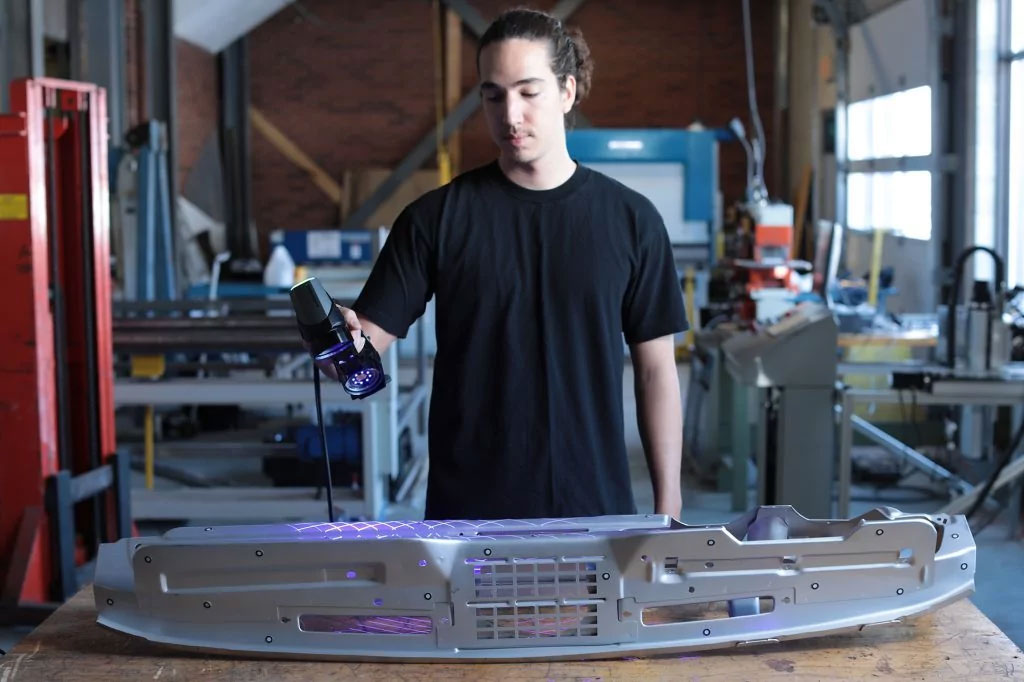 An employee with a black shirt in a workshop using a HandySCAN 3D|BLACK to scan a stamped metal part with sharp and hemmed edges
