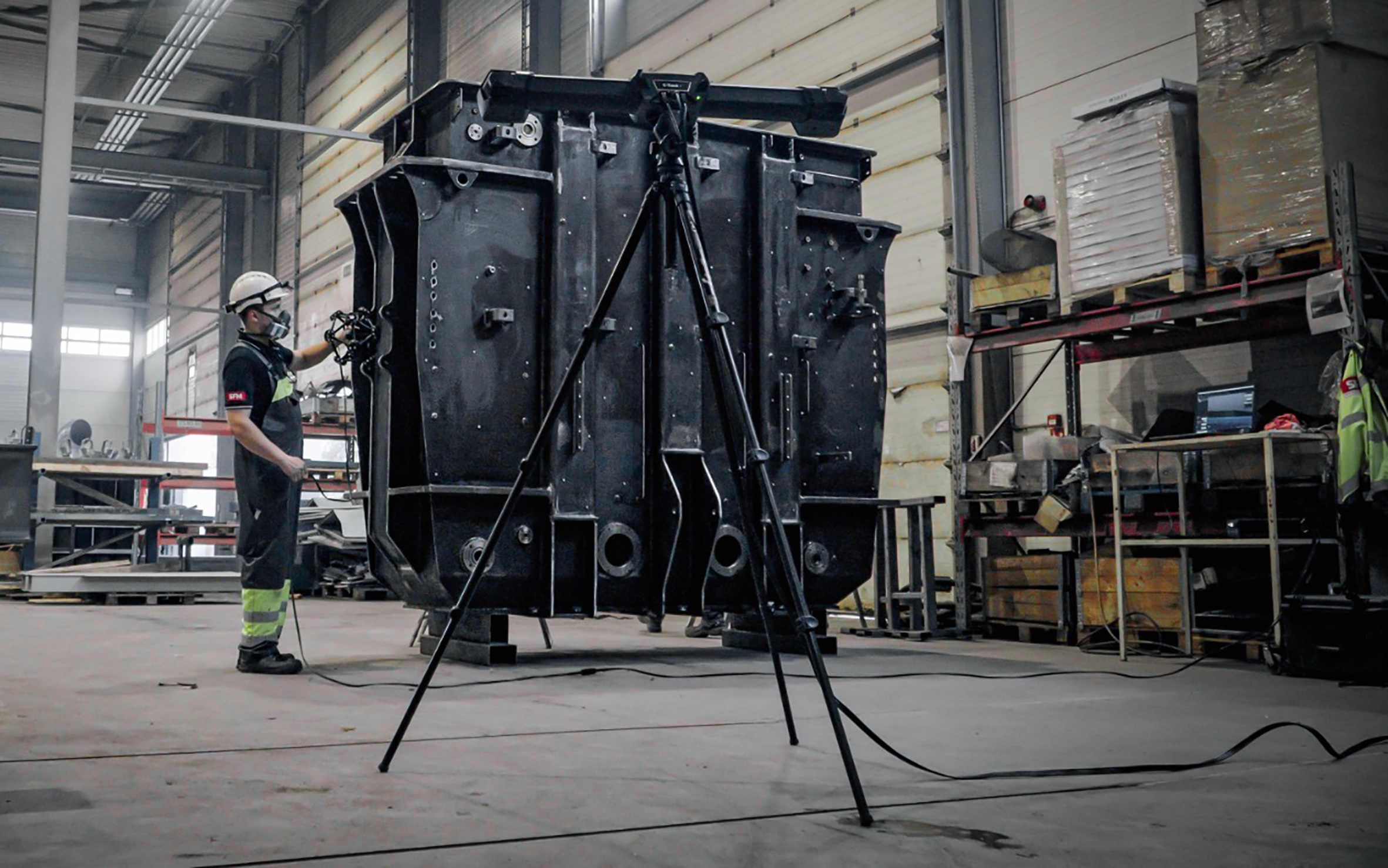SFM employee wearing a white helmet and a respirator, using a MetraSCAN 3D to scan a transformer tank, with a C-track in the foreground