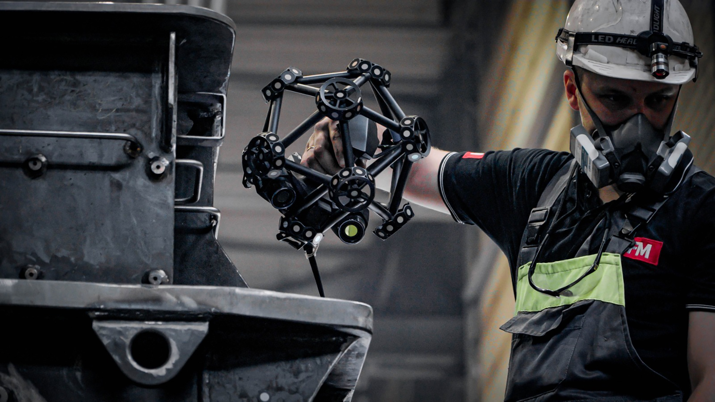 Close up of SFM employee wearing a white helmet and a respirator, using a MetraSCAN 3D to scan a transformer tank