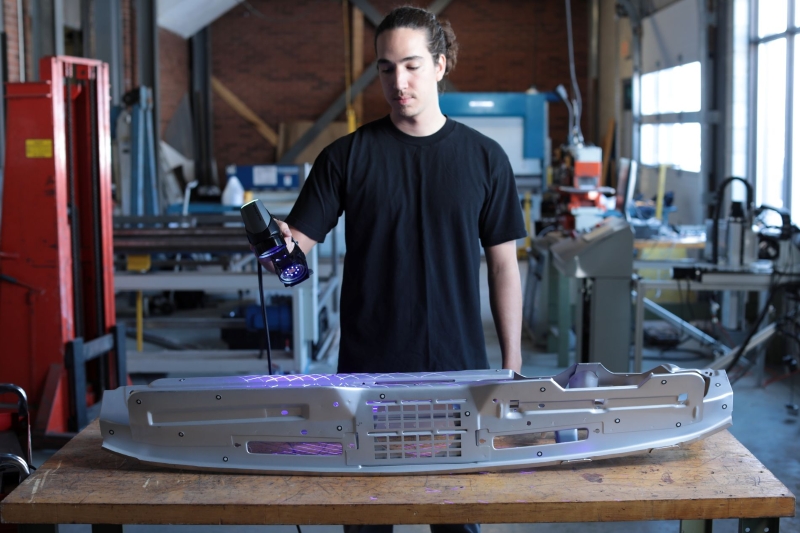 Person scanning a large metallic object with a handheld 3D scanner in an industrial workshop