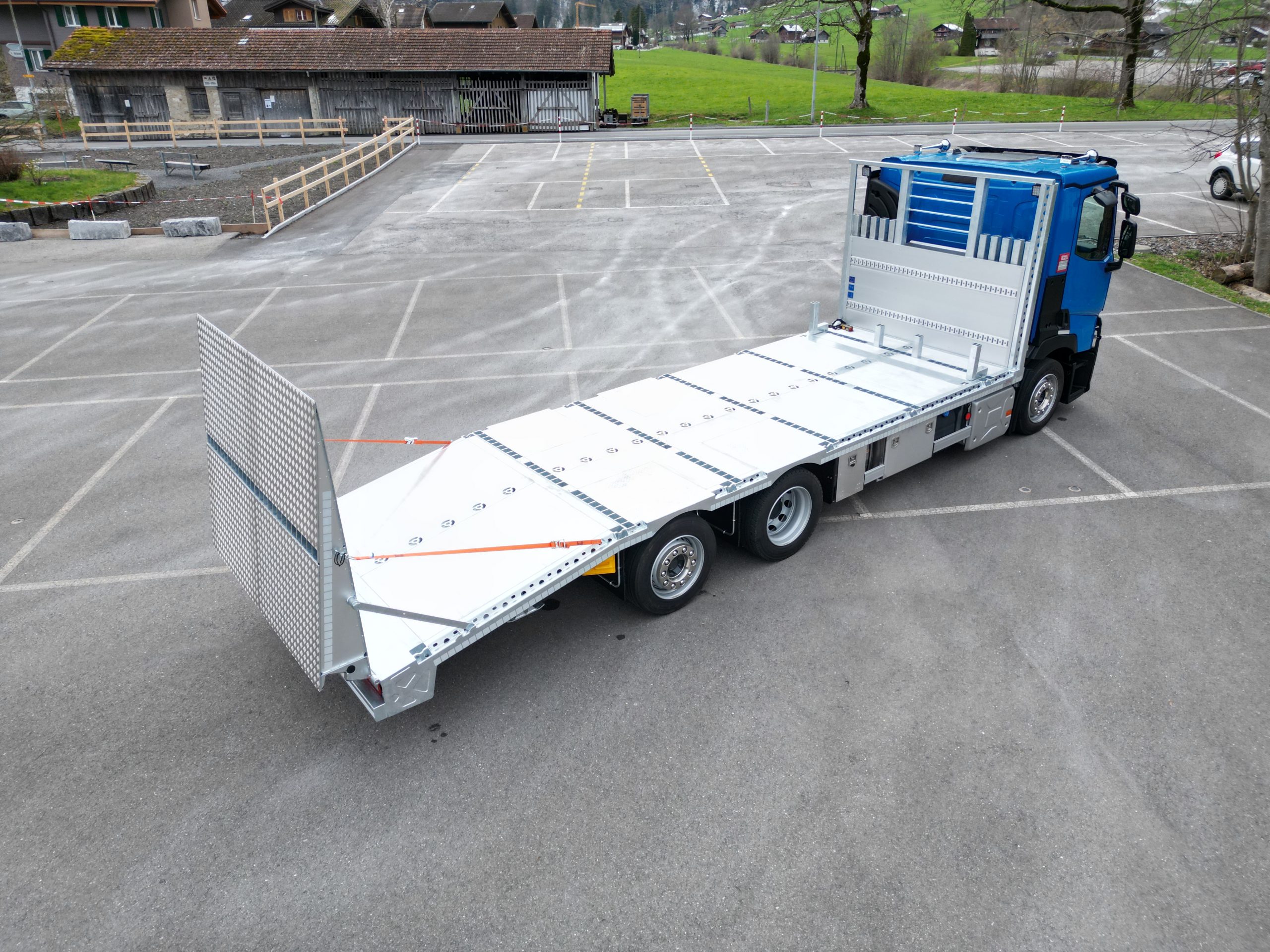 一辆被称为工程机械出租车的卡车停在院子里。这辆工程机械出租车出于空载状态。驾驶室为蓝色,装载区域为铝色。