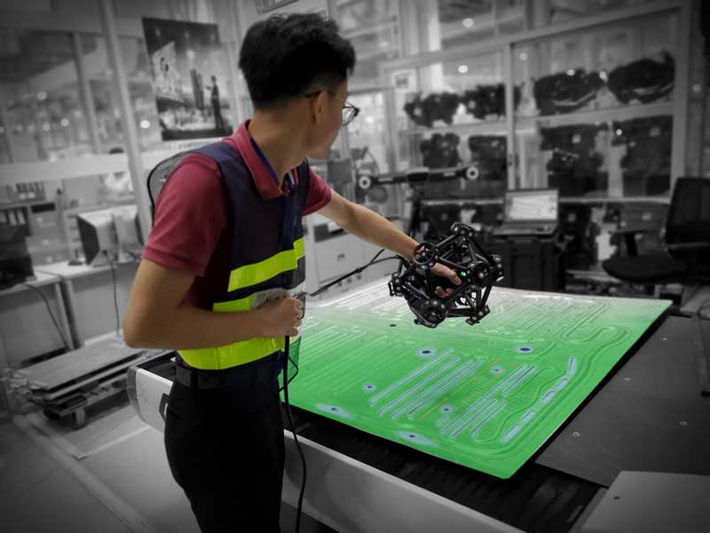 Funcionário vestindo um colete de segurança usando um scanner MetraSCAN 3D para medir uma peça de chapa metálica plana com sobreposição de mapa de cores