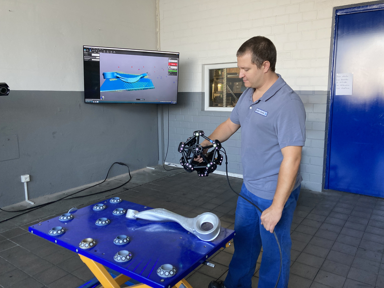 An employee scans a metal part using the MetraSCAN 3D optical CMM scanner.