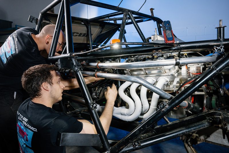 Due meccanici di EP9 Autosport che installano un nuovo collettore sul motore di un'auto da corsa all'interno del telaio del veicolo.