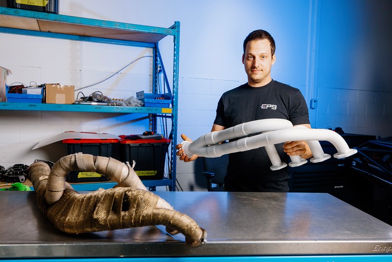 An EP9 Autosport mechanic comparing the ceramic thermal coating manifold with the old wrapped version on a workbench in the workshop.
