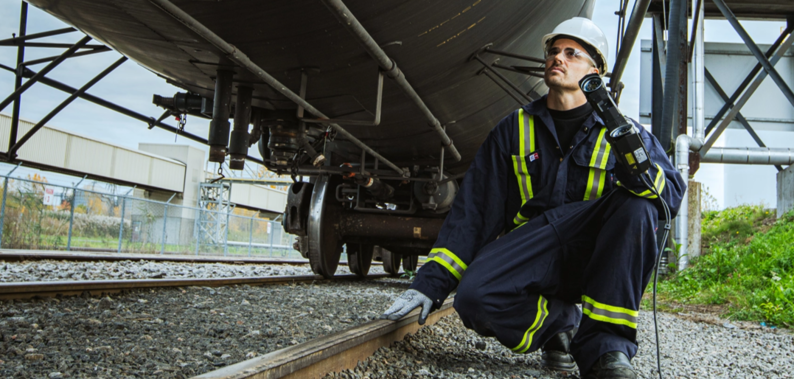 Photograph of a freight train on railway tracks, with a technician scanning the cars using a 3D scanner