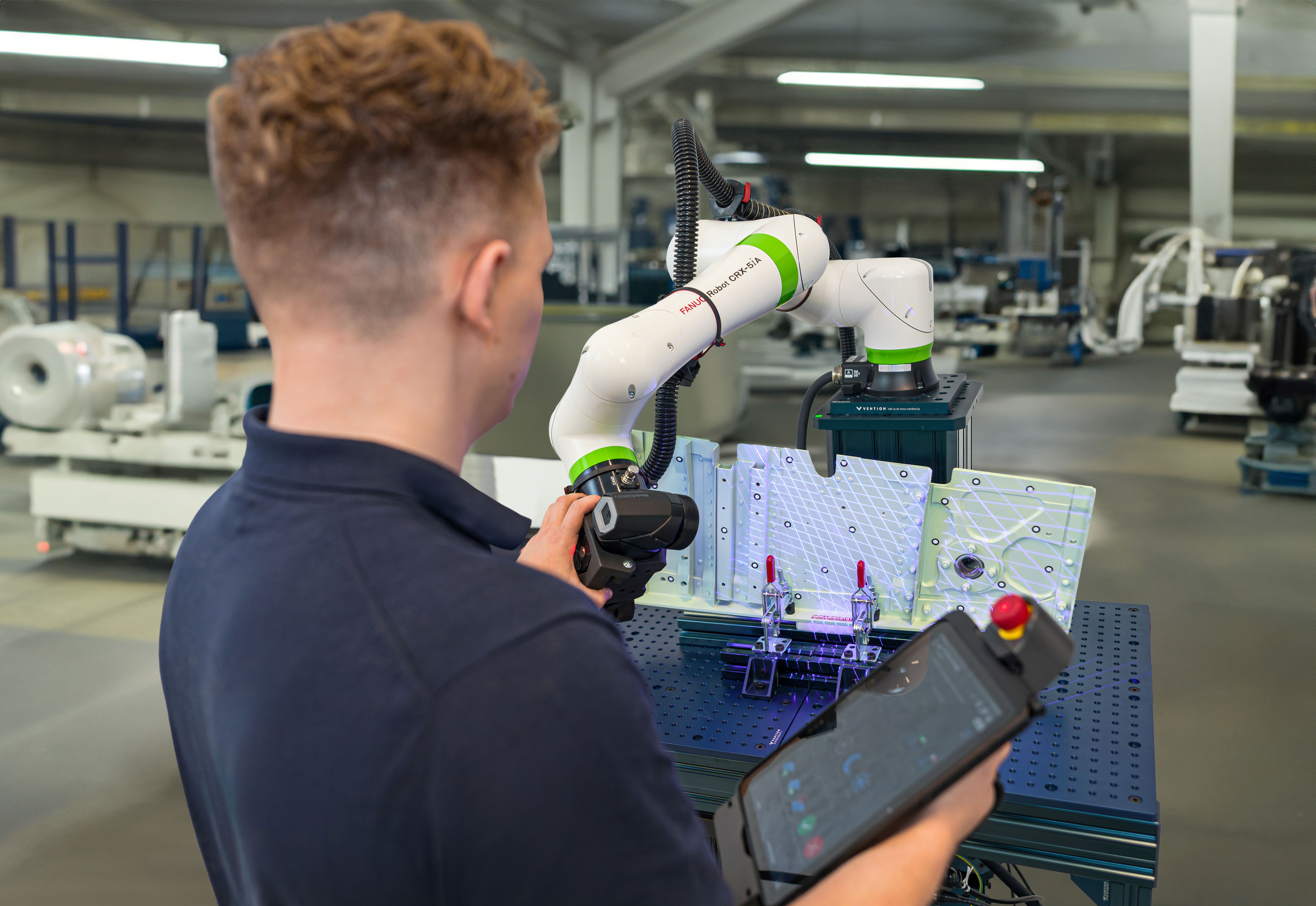 Technician guiding a HandySCAN BLACK+ mounted on a cobot from the Automation Kit to scan a complex aerospace component, using the teach pendant to record robot paths within the Automation software module of Creaform Metrology Suite. 