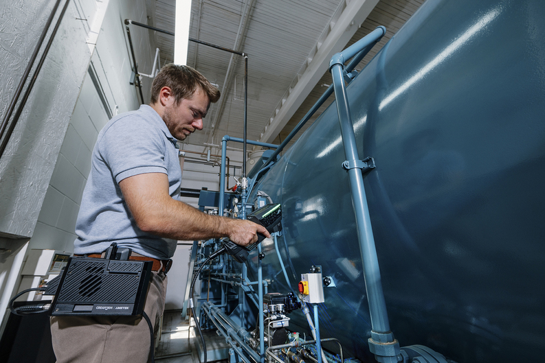 Operatore che ispeziona un grande serbatoio industriale con uno HandySCAN 3D|Serie EVO e il Kit mobilità in ambiente di produzione, vicino a vibrazioni e in spazi stretti.