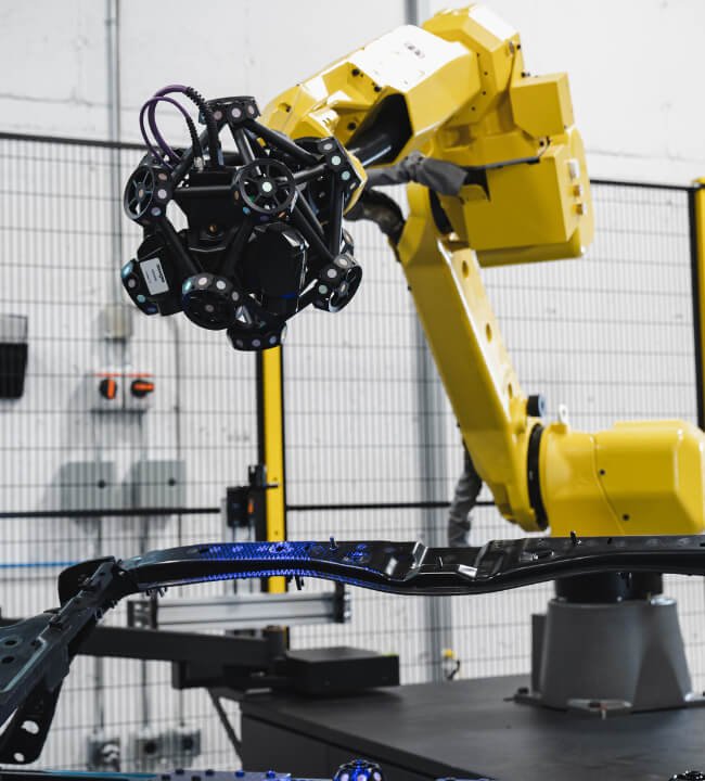 Industrial robot equipped with a Creaform MetraSCAN 3D scanner performing precise measurements on a metal automotive part in a high-tech manufacturing facility.