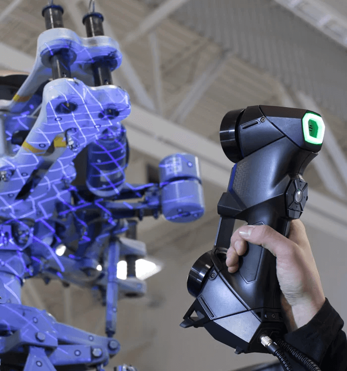 Technician using a Creaform HandySCAN 3D scanner to capture detailed measurements of a complex suspension system, with laser grids highlighting the scanned surfaces.