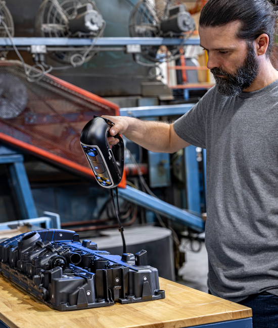 Expert using PRO Series 3D scanner projecting blue laser lines on a plastic engine cover in a manufacturing setting