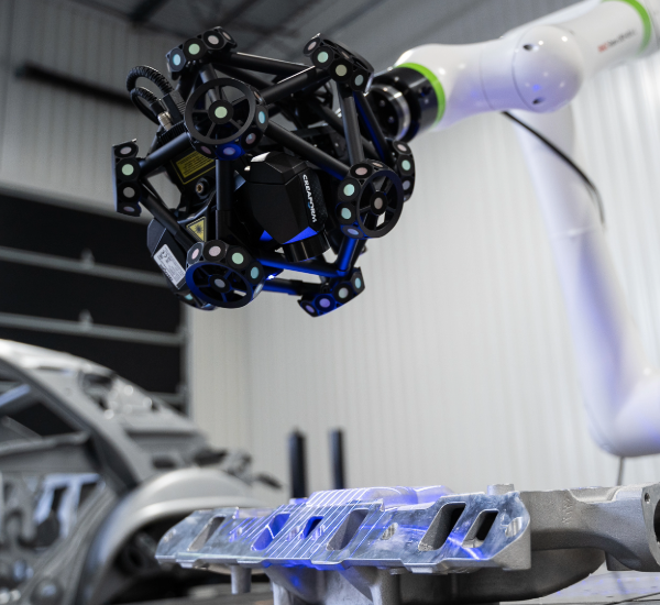 White robot holding a MetraSCAN 3D-R scanning a manifold casting and blue laser lines projected in the part