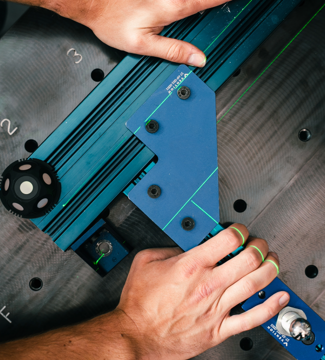Hands adjusting a jig with green laser alignment lines on a perforated metal surface