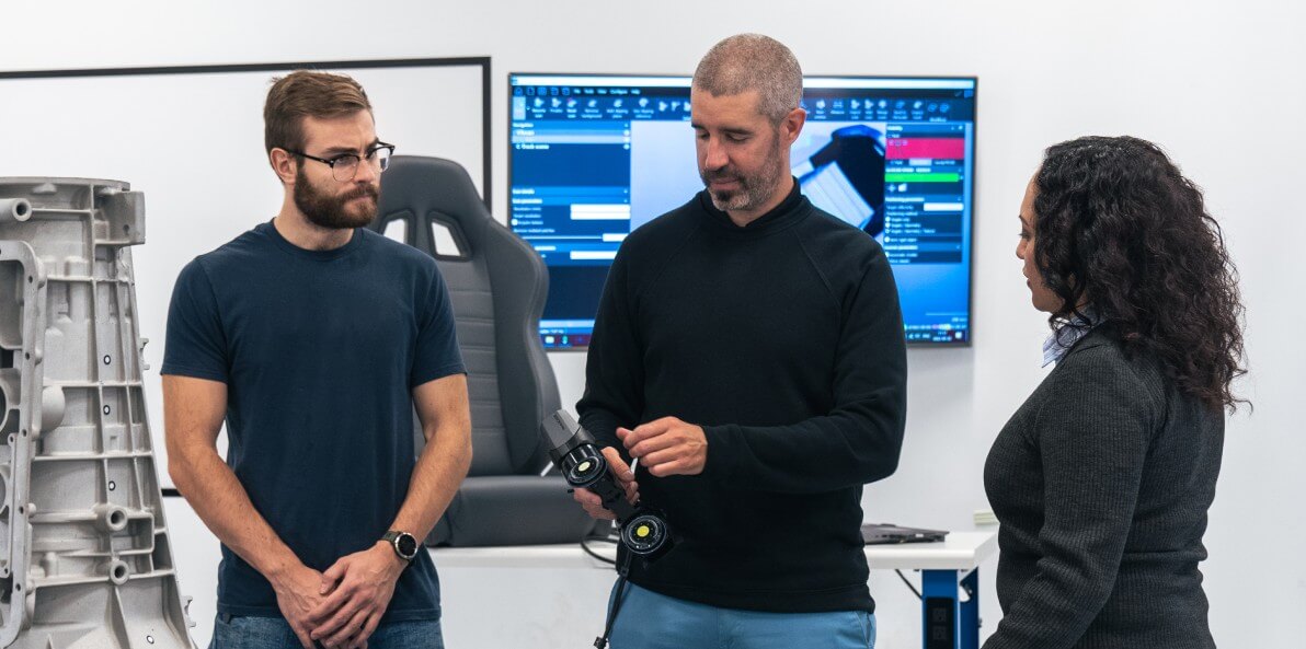 Group of professionals discussing the features of a Creaform 3D scanner in a modern workspace.