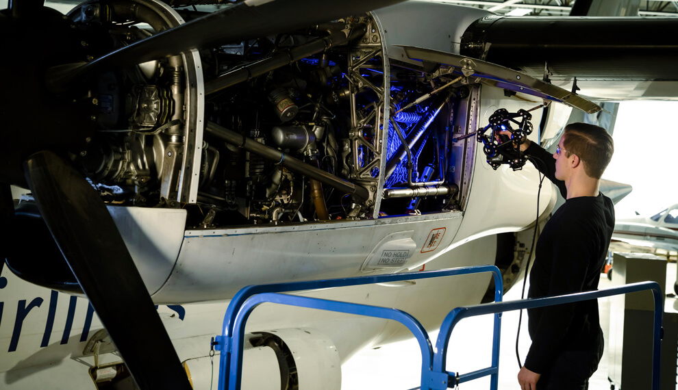 Technician using a Creaform MetraSCAN 3D scanner to inspect the intricate engine components of an aircraft, with laser grids highlighting the scanned areas.