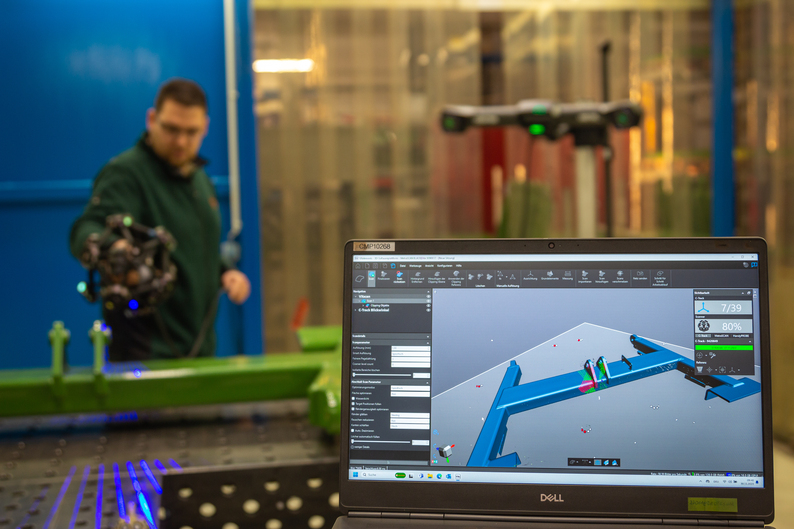Ein detailliertes Netz eines großen Teils erscheint in Echtzeit auf einem Computer, während ein Ingenieur es mit dem MetraSCAN 3D scannt.