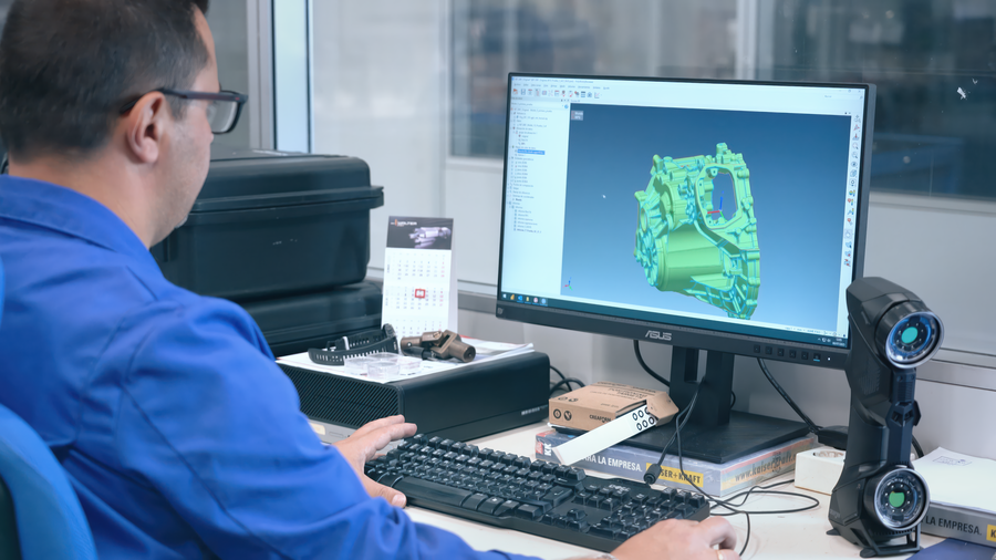 Engineer analyzing a 3D scan of an automotive casting on a computer screen using the PolyWorks metrology software, with a HandySCAN 3D on the desk