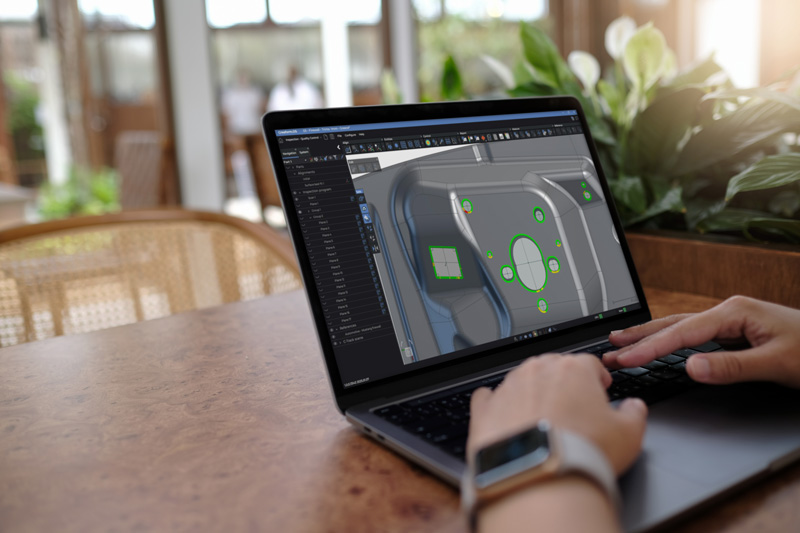 Someone sitting at a table using a laptop displaying a part in the Inspection module of the Creaform Metrology Suite