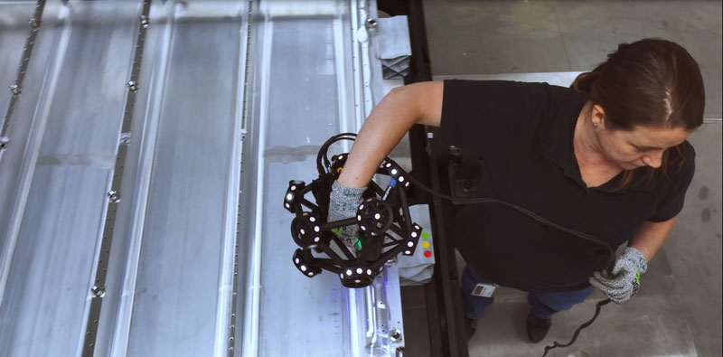 Vista dall'alto di un dipendente che utilizza lo scanner 3D MetraSCAN per ispezionare il vassoio della batteria di un'automobile