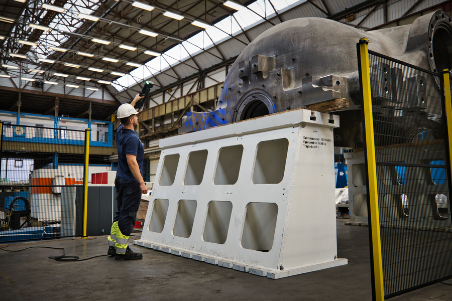Employee wearing a hard hat using the HandySCAN 3D|MAX Series scanner to measure a large water turbine cover in a warehouse.