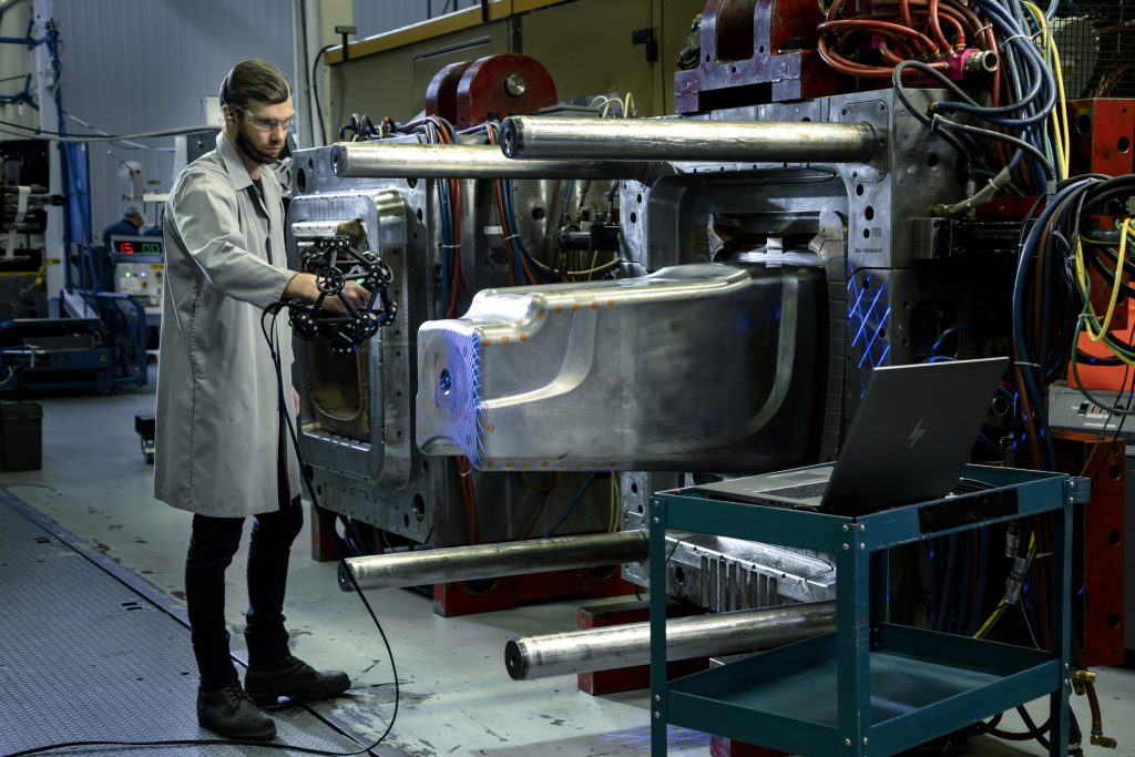 Metrology technician operating a blue light handheld 3d laser scanner on a large industrial mold in a factory environment