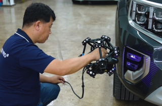 Employee using the MetraSCAN 3D scanner to scan the front bumper of a blue-grey car