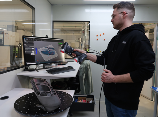 Man scanning with the HandySCAN SILVER an exhaust finisher for the Bugatti Chiron. In the background is a laptop showing the 3D scan in real-time in the VXelements software