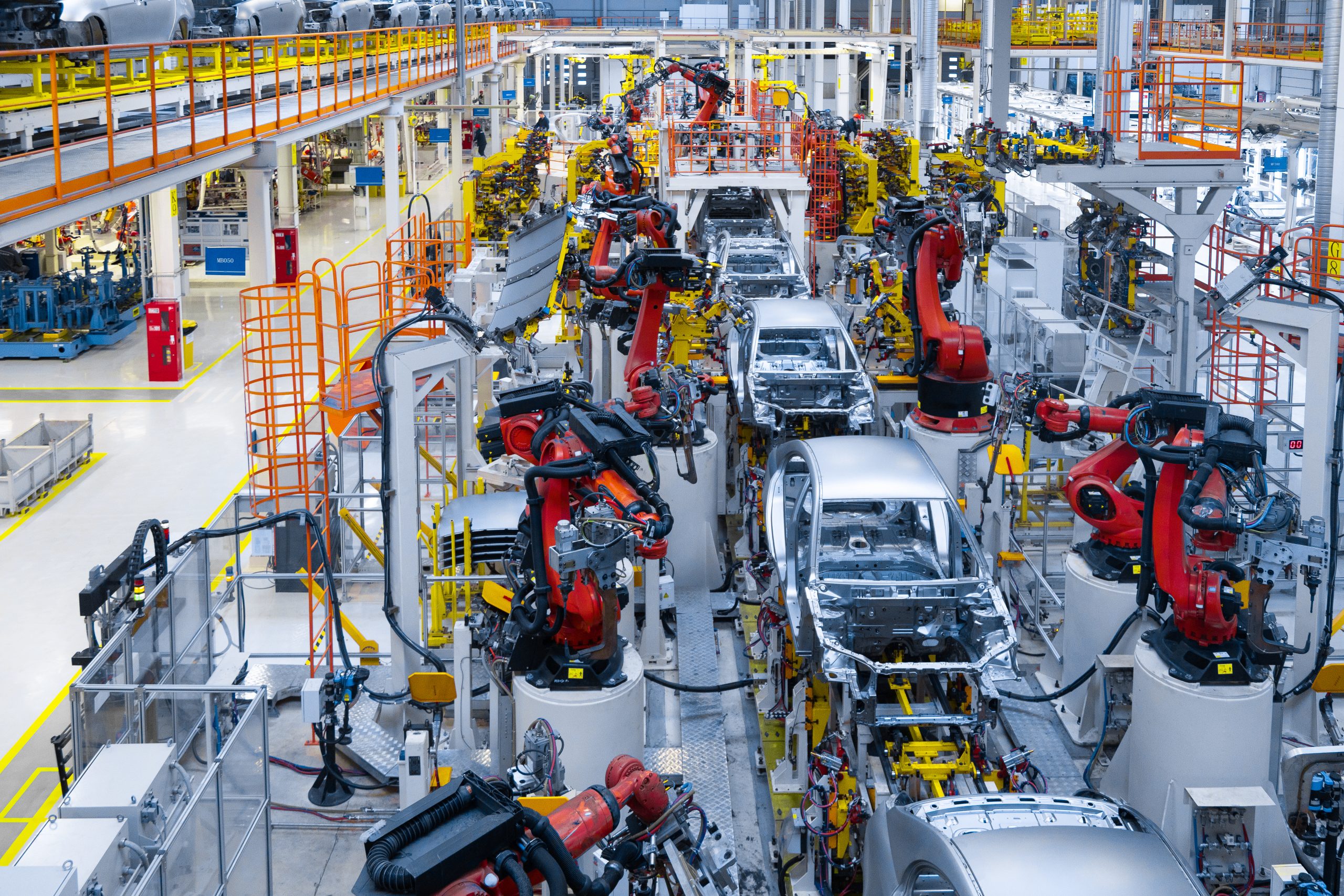 Several red and yellow robot arms assembling a row of cars on an assembly line inside a factory