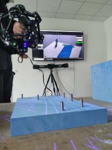 Überprüfung der richtigen Positionierung der Bohrungen an einem Modell, eine typische Anwendung des MetraSCAN 3D bei Blacks. Im Hintergrund ist das optische Kamerasystem C-Track zu sehen. Der Scan wird in Echtzeit auf dem Bildschirm angezeigt.