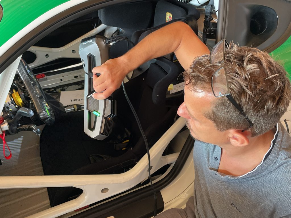 Homme avec une chemise grise utilisant le scanner Go!SCAN 3D pour numériser l'intérieur du cockpit d'une Porsche Cayman GT4 blanche