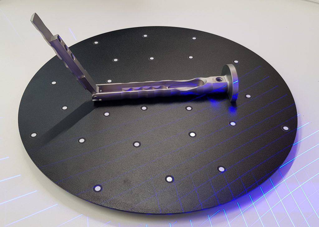 Poignée chirurgicale posée sur une table tournante noire, avec des cibles collées. On voit des lignes laser bleues.