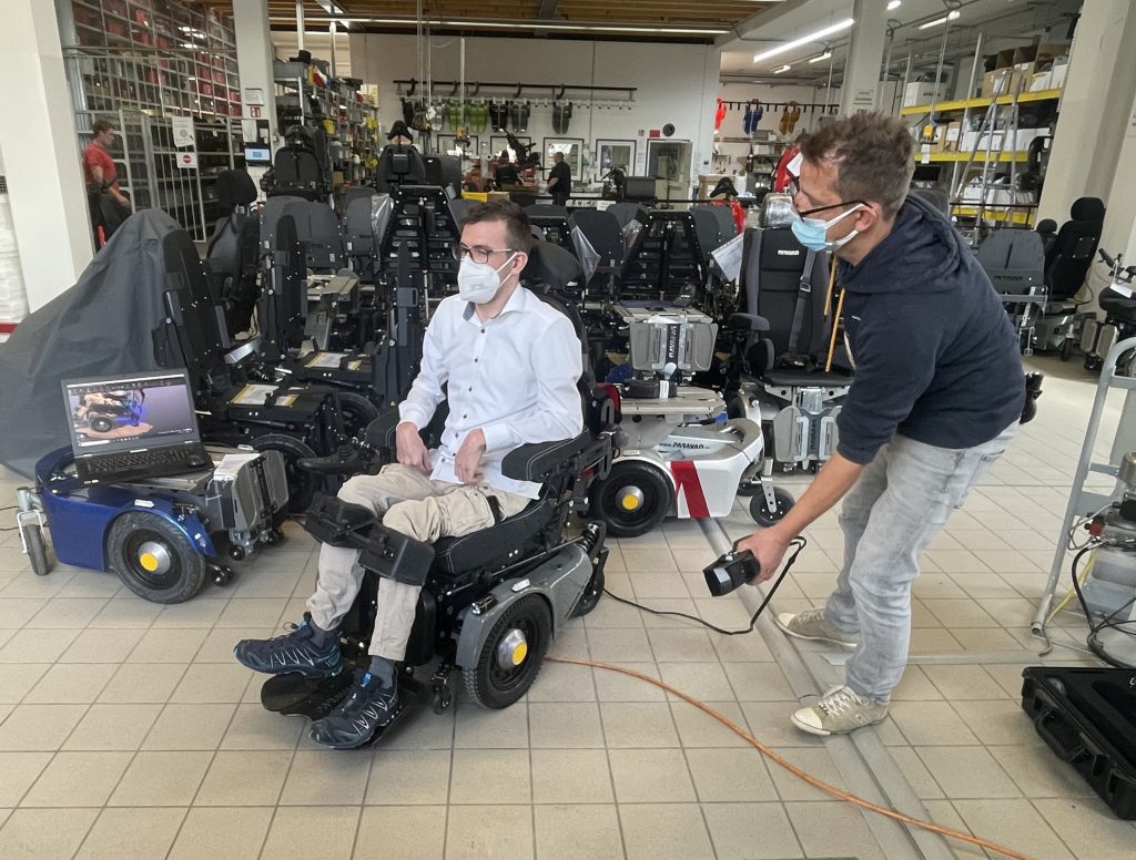 Hombre usando el escáner Go!SCAN 3D para escanear a una persona en silla de ruedas con varias sillas de ruedas en el fondo