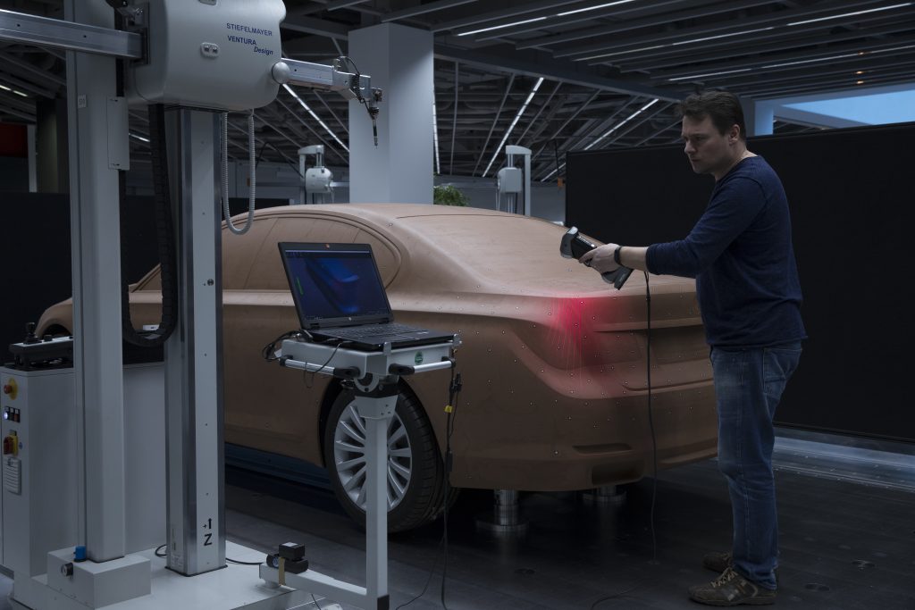 Employee using a HandySCAN 3D scanner to scan a clay model of a BMW car inside a warehouse