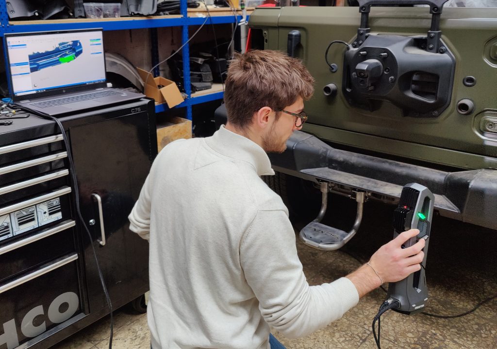 An employee of AADS scanning a Jeep bumper with the Go!SCAN SPARK with a laptop in the background displaying the visualized data in real time in VXelements acquisition software.