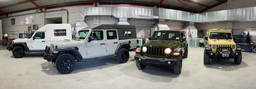 White, grey, green, and yellow jeeps lined up in a hall.