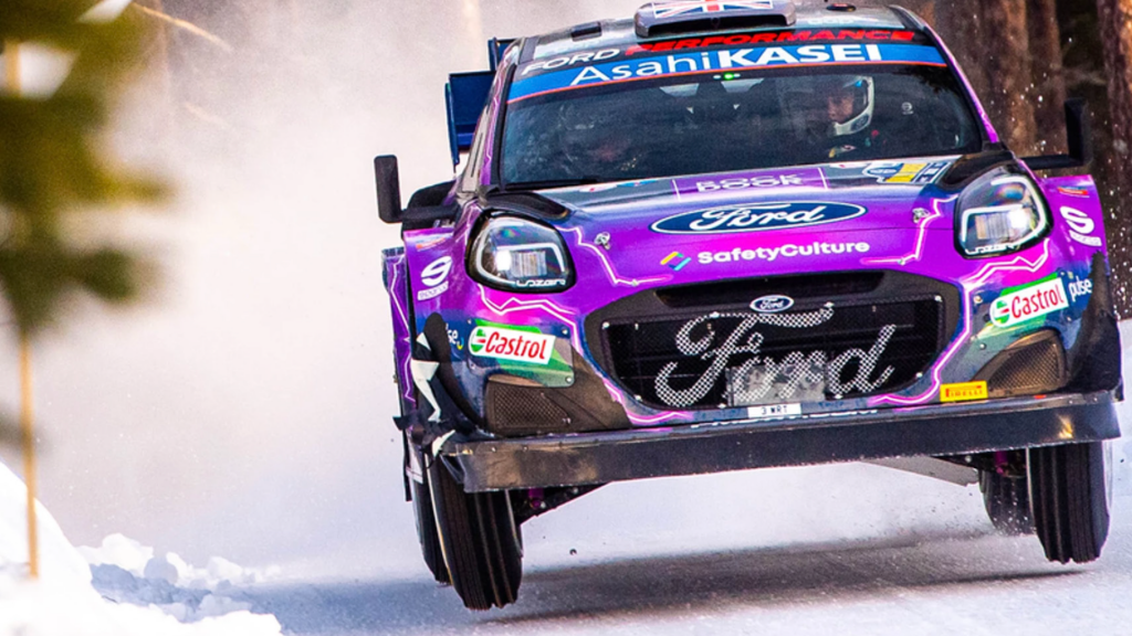 Purple Ford rally car with decals driving fast on snow track
