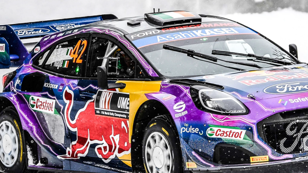 Purple Ford rally race car with decals taking a fast turn on a snow track