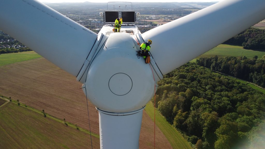 Two employees working on top of the rotor of a wind turbine