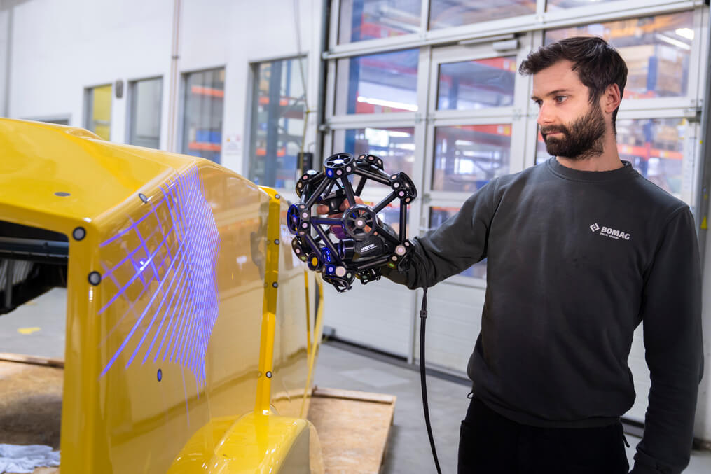 Collaboratore Bomag che misura un componente giallo di grandi dimensioni con lo scanner MetraSCAN 3D