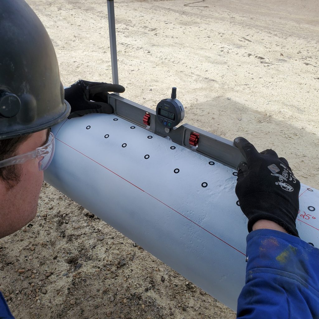 Employee with hard hat assessing Corrosion Depths of a pipeline with pit gauge